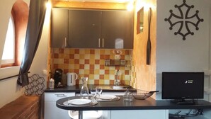 A compact kitchen with a checkered backsplash, a coffee machine, and a TV on a stand.