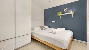 Ein Schlafzimmer mit einem Bett, weißer Bettwäsche, einer blauen Akzentwand, einem Regal mit Dekoration und einem weißen Kleiderschrank.