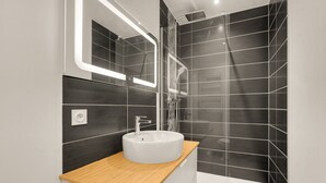 Ein modernes Badezimmer mit einem Holz-Waschtisch, einem weißen Waschbecken, einem Spiegel und einer Duschkabine.
