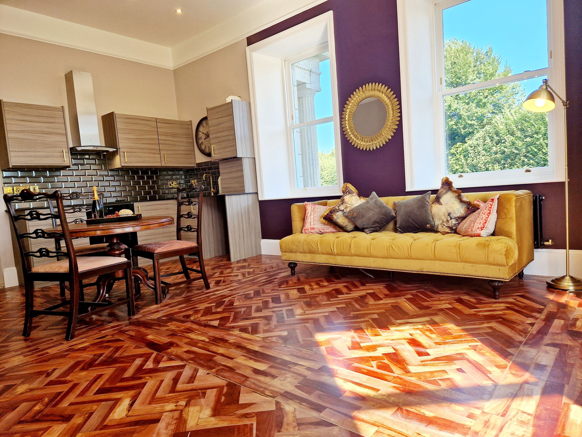 A modern kitchen with wooden cabinets, a herringbone-patterned floor, and a yellow sofa with decorative pillows.