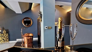 Una zona de bar con un mezclador de cócteles de cobre, una botella de champán y copas sobre una mesa negra con detalles dorados.