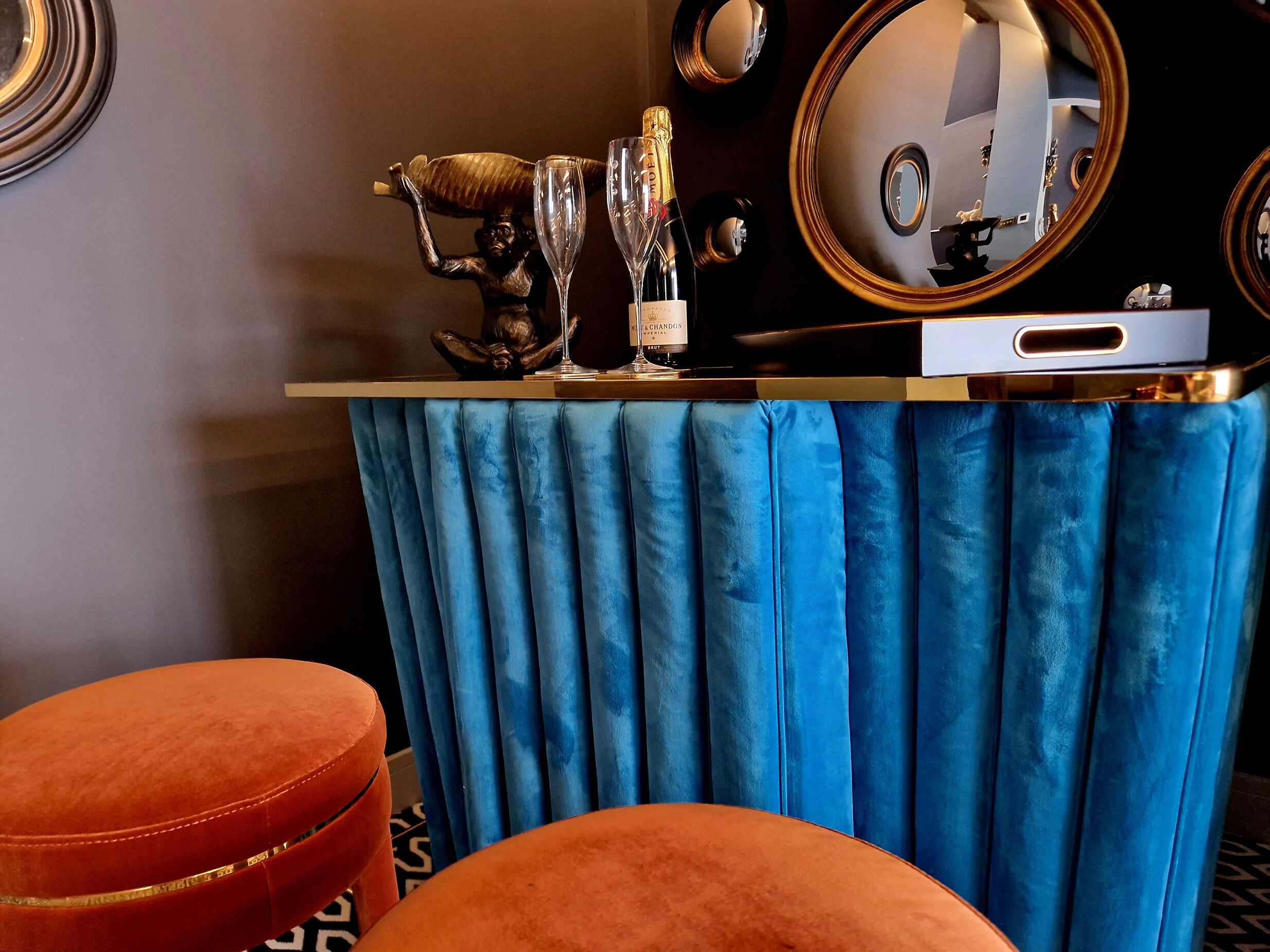 Une coiffeuse recouverte d’un drap de velours bleu, avec un miroir et une bouteille de champagne.