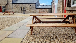 Un patio al aire libre con paredes de piedra, una mesa de picnic de madera y una fuente de piedra.