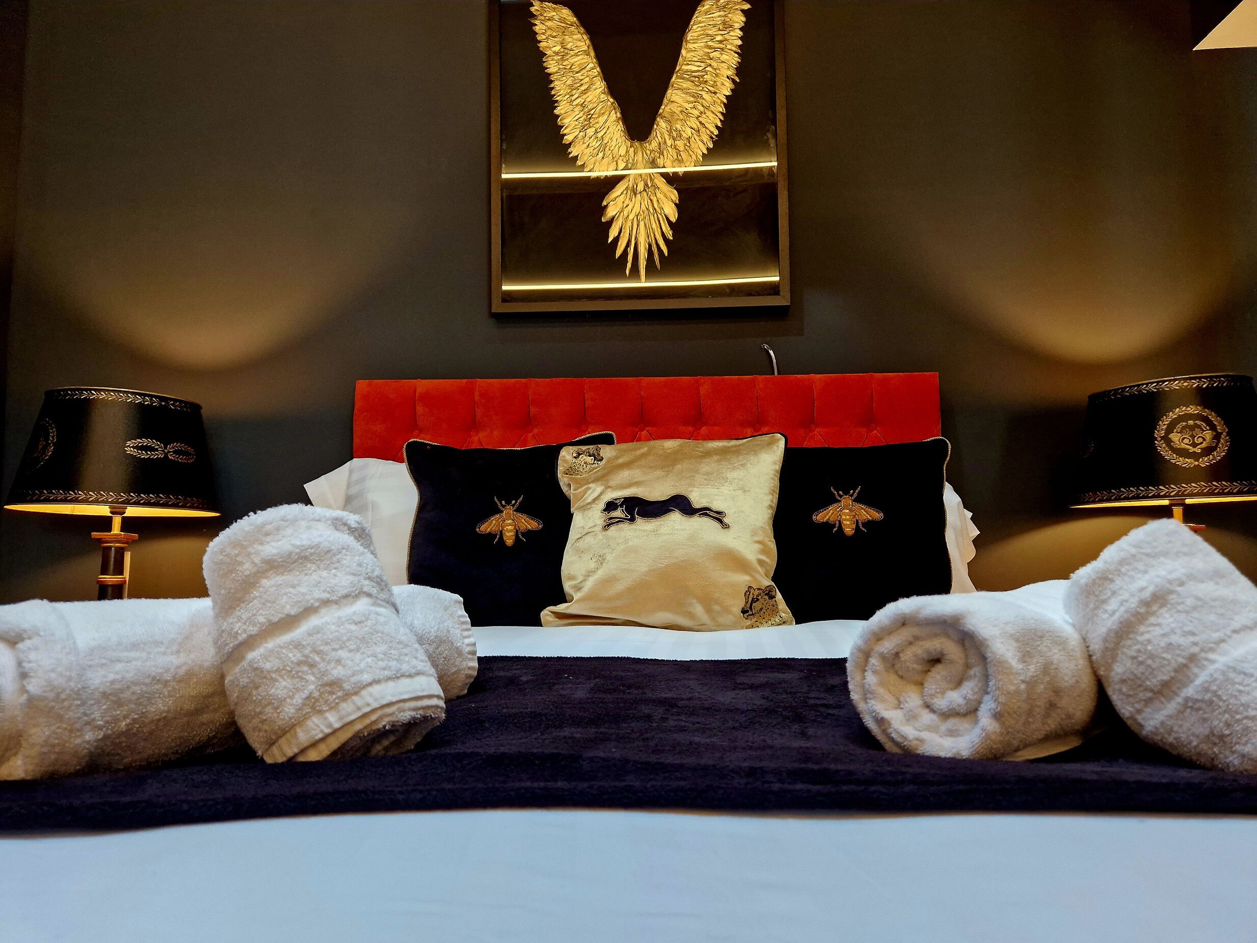 A hotel room with a bed, two lamps, a red headboard, and a wall-mounted golden emblem.