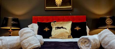 A hotel room with a bed, two lamps, a red headboard, and a wall-mounted golden emblem.