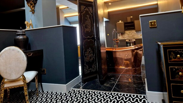 Habitación de hotel moderna con una pared de acento azul oscuro, piso estampado y vista al área de la cocina.