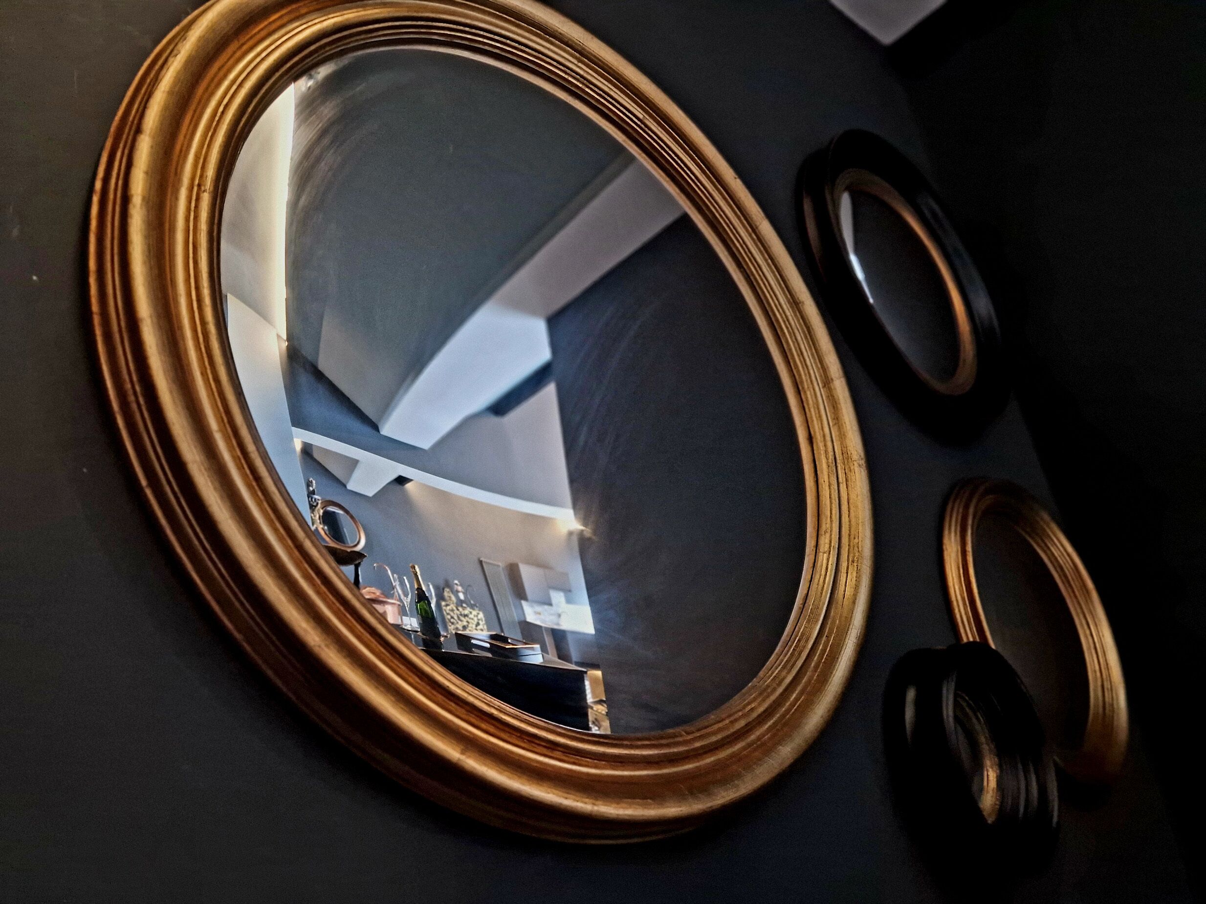 Ein goldgerahmter Spiegel, der einen Raum mit moderner Decke und einen kleinen Tisch mit Gegenständen darauf reflektiert.