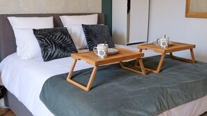 A neatly made bed with a grey blanket and two wooden nightstands, each holding a white mug with a black pattern.
