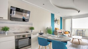 Una cocina moderna con horno empotrado, un comedor con sillas azules y un espacio de sala de estar con sofá y una mesa de centro.