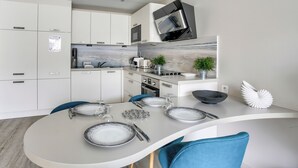 Una cocina moderna con armarios blancos, microondas integrado y un comedor con mesa curva y sillas azules.