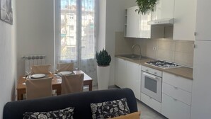 Eine moderne Küche mit weißen Schränken, einem Gasherd und einer Spüle. Ein Essbereich mit Tisch und Stühlen lädt zum Verweilen ein, und ein Fenster bietet Blick auf die Stadt.