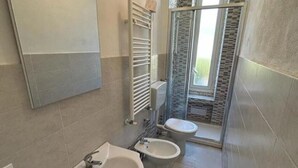 Ein modernes Badezimmer mit einem großen Spiegel, einem Waschbecken, zwei Toiletten und einer Duschkabine.