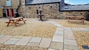 A stone building with a gravel courtyard, two picnic tables, and a fountain. - Alexander (Preston)