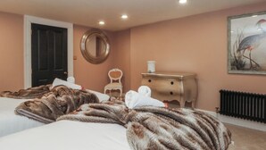 A hotel room with two beds, a round mirror, a white chair, a nightstand with a lamp, and a radiator. - Alexander (Preston)