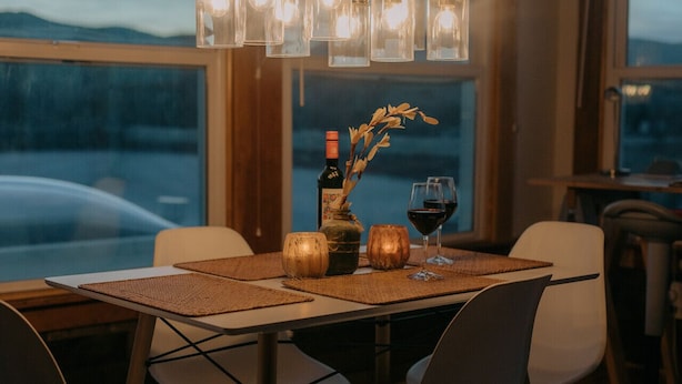 Une table à manger avec des sets de table, une bouteille de vin et un verre de vin, le tout placé devant une fenêtre offrant une vue sur les montagnes.