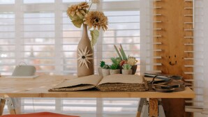 Une table en bois sur laquelle repose un livre ouvert, un vase contenant des fleurs séchées et de petites plantes en pot.