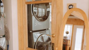 Une buanderie avec des machines à laver superposées, une serpillière et une porte en bois dotée d’une vitre.