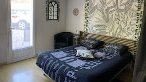 A bedroom with a bed, a chair, a window, and a wall with a plant and leaf pattern.