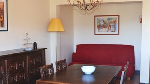 A dining area with a wooden table, chairs, a red sofa, a lamp, and a painting on the wall. - Bel Appartement T2 Avec Balcon Donnant Plein sud sur la Chaîne des Pyrénées (Font-Romeu-Odeillo-Via)