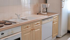 A kitchen with wooden cabinets, a white countertop, a built-in oven, and a refrigerator. - Bel Appartement T2 Avec Balcon Donnant Plein sud sur la Chaîne des Pyrénées (Font-Romeu-Odeillo-Via)