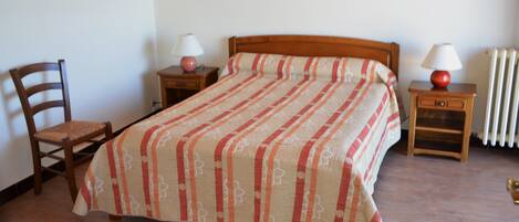 A bedroom with a bed, two bedside tables, a chair, and a radiator.