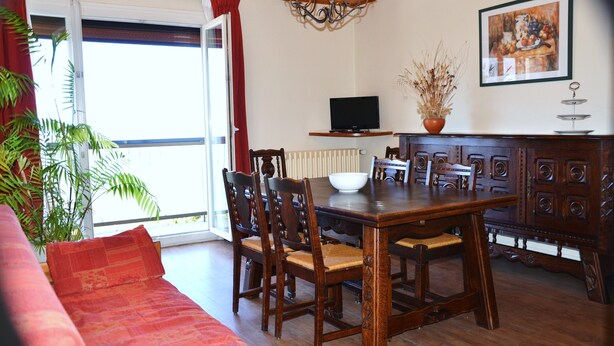 A dining area with a wooden table, chairs, a television on a shelf, and a potted plant. - Bel Appartement T2 Avec Balcon Donnant Plein sud sur la Chaîne des Pyrénées (Font-Romeu-Odeillo-Via)