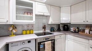 Une cuisine moderne avec des meubles blancs, un lave-linge encastré, une machine à café et une bouilloire.