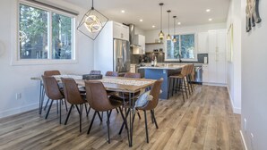 A modern kitchen with white cabinets, a central island, and pendant lighting. - Cozy duplex on ski way with private hot tub, laundry, garage and large ski room! (Silver Star Mountain)