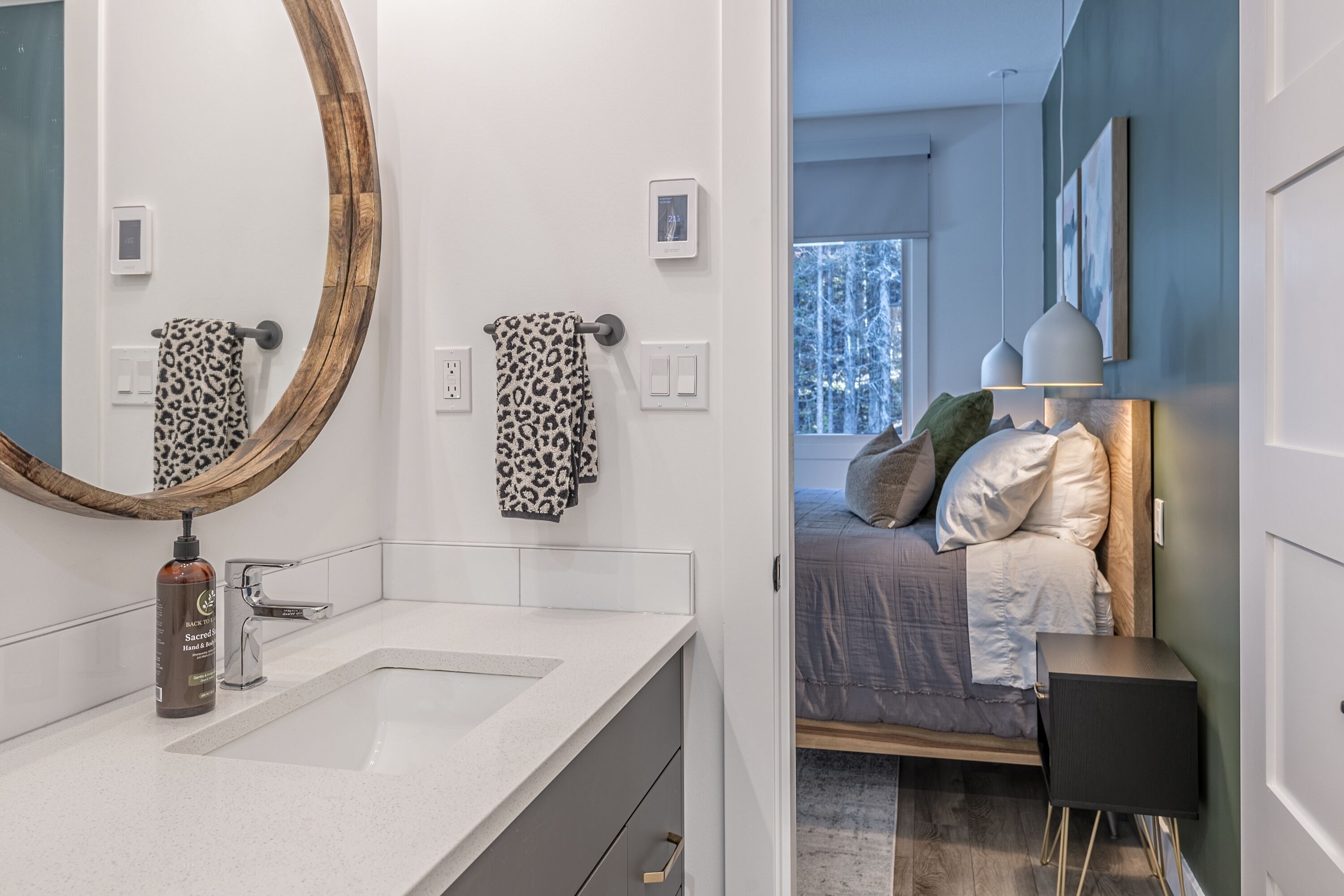 A modern bathroom with a large mirror, two leopard print towels, a bottle of hand soap, and a white sink.