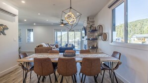 A dining area with a large wooden table, six brown chairs, and a geometric pendant light. - Cozy duplex on ski way with private hot tub, laundry, garage and large ski room! (Silver Star Mountain)