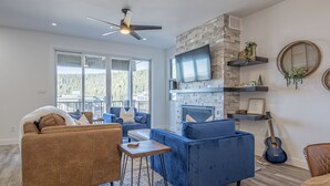 A modern living room with a brown sofa, blue armchair, and a coffee table. - Cozy duplex on ski way with private hot tub, laundry, garage and large ski room! (Silver Star Mountain)