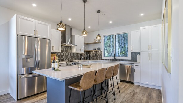 A modern kitchen with a central island, stainless steel appliances, and pendant lighting. - Cozy duplex on ski way with private hot tub, laundry, garage and large ski room! (Silver Star Mountain)