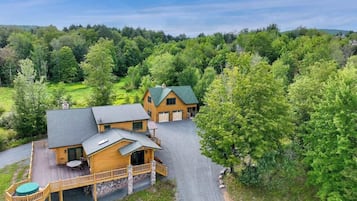 Une grande cabane en bois dotée d’une terrasse, d’un patio couvert et d’une allée menant à un garage.