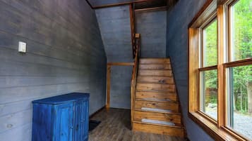 Un intérieur en bois avec un escalier, une armoire bleue et une fenêtre donnant sur un paysage verdoyant.