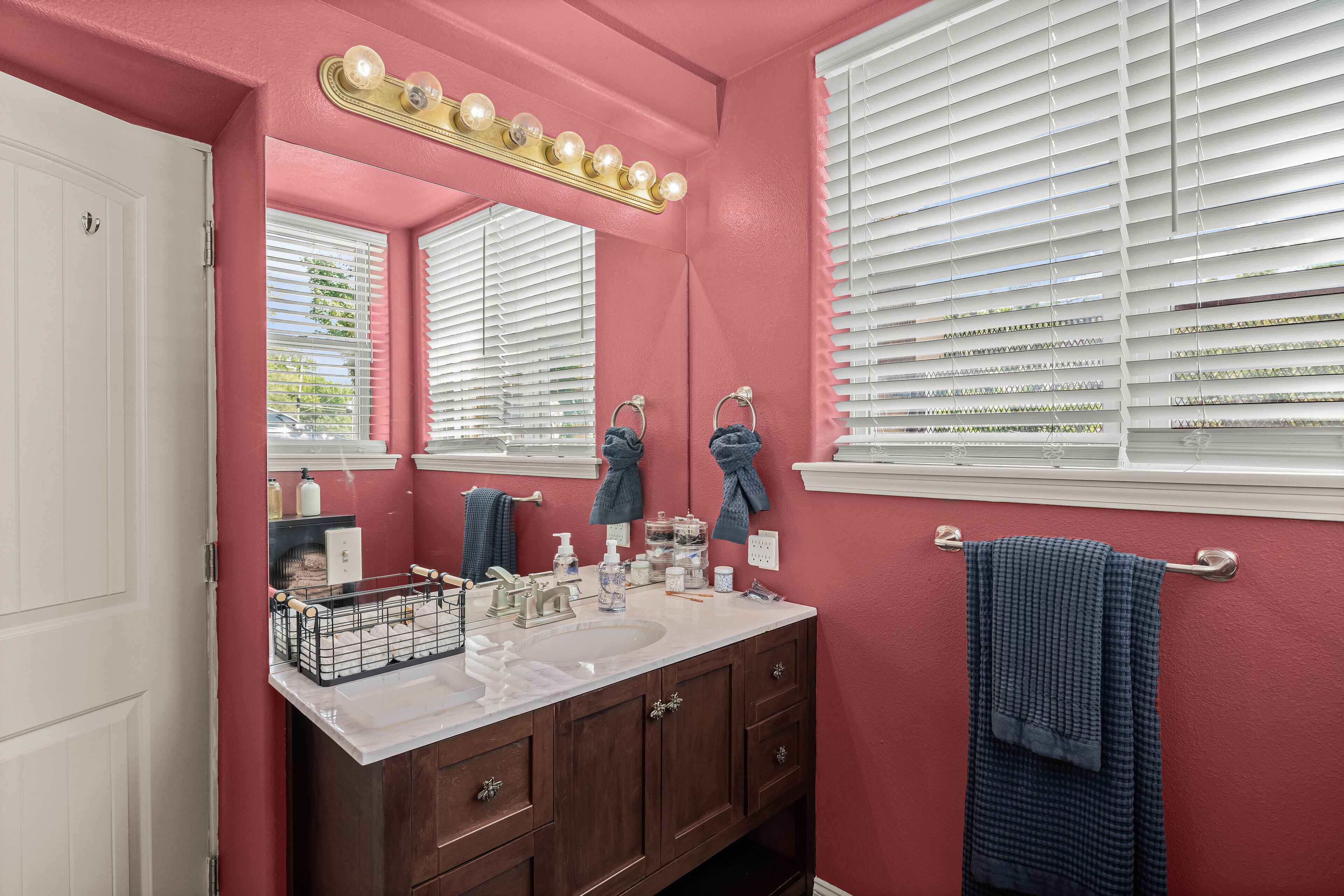 A bathroom with a pink wall, a white sink, and a vanity with a mirror.