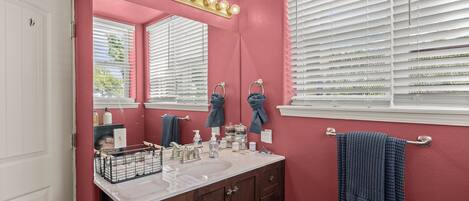 A bathroom with a pink wall, a white sink, and a vanity with a mirror.
