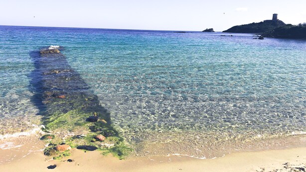 A clear coastal view with a sandy beach, rocky outcrops, and a distant hill with a structure. - A casa di Oba, vacation home a stone's throw from the sea in Nora, Pula, Sardinia (Pula)