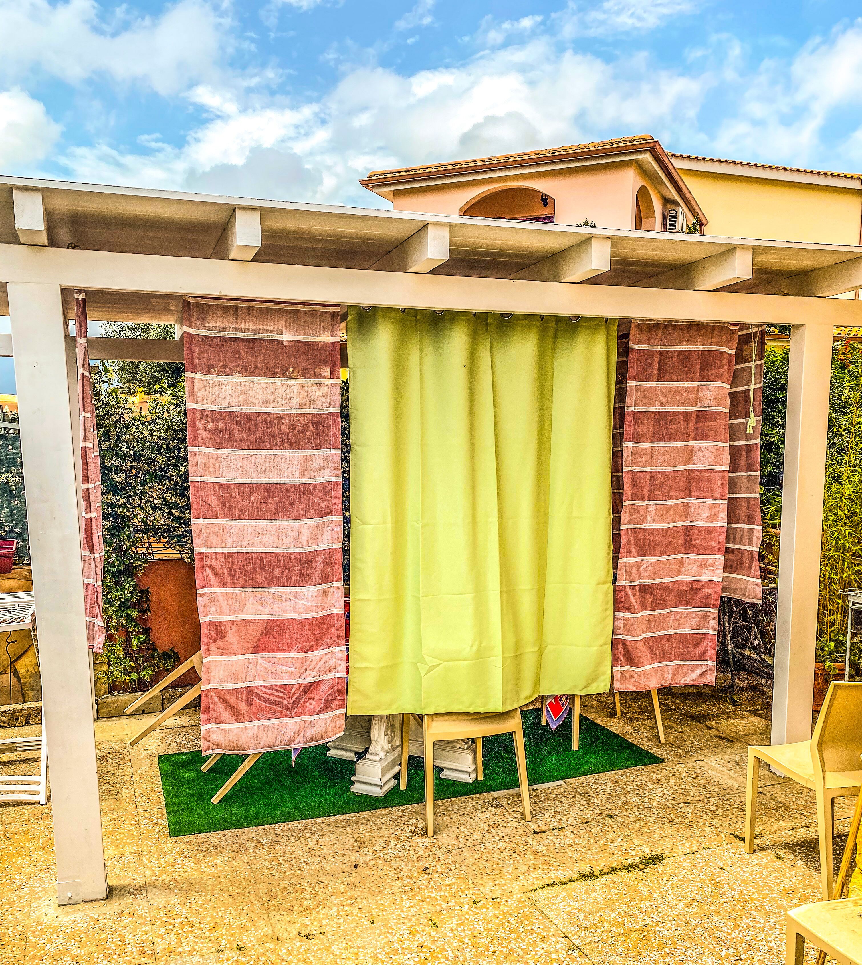 A covered outdoor area with a pergola structure, a green curtain, and a red and white striped curtain.