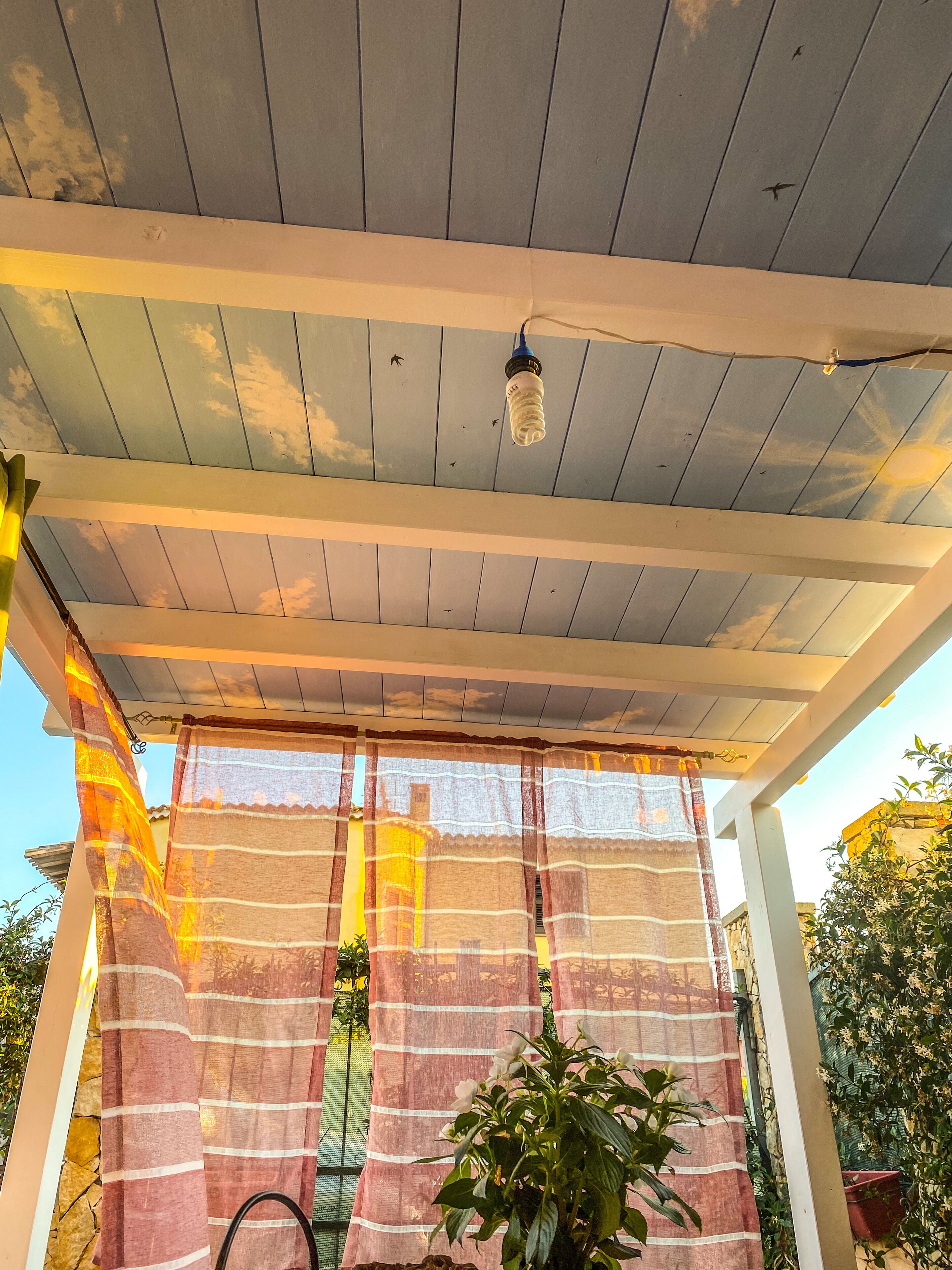 A covered outdoor area with a ceiling fan, striped curtains, and potted plants.