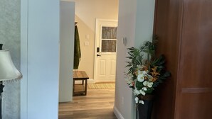 A hallway with a wooden floor, a door with a frosted glass panel, and a potted plant with white flowers. - Cottage/Studio in Cobble Hill Village - hiking, wineries and more (Cobble Hill)