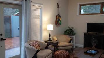 Un salon avec une porte donnant sur un patio, une lampe, une guitare, un téléviseur et une plante.