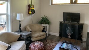 A living room with a sofa, a chair, a table with a lamp, a guitar, a TV, and a plant. - Cottage/Studio in Cobble Hill Village - hiking, wineries and more (Cobble Hill)
