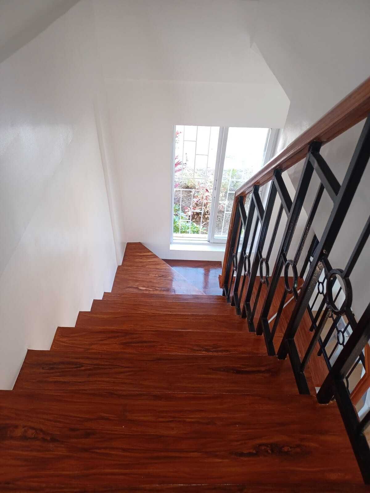 Un escalier en bois avec des rampes noires menant à une porte en verre.