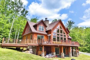 A log cabin with a balcony, stone foundation, and a large window.