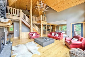 A spacious living area with a fireplace, red leather sofas, a coffee table, and a staircase leading to an upper level.