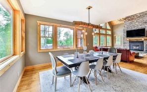 A spacious dining area with a large table and chairs, a fireplace, and a stone wall.