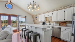 A kitchen with white cabinets, a stone accent wall, a chandelier, and a bar area with stools.
