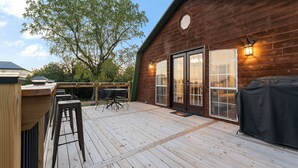 A wooden deck with a table and chairs, a barbecue grill, and a large window with a view of trees.