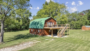 A wooden cabin with a green roof, a deck, and a staircase leading to a balcony.
