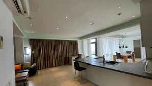 A modern kitchen with a central island, a dining area with a table and chairs, and a living space with a sofa and curtains. - Apartment With Ocean View (Accra)
